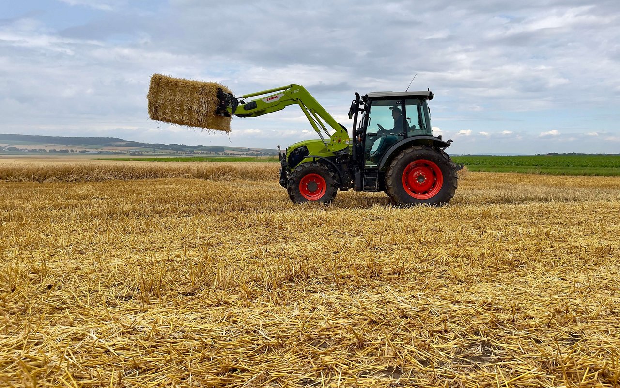 Claas Elios mit einem Strohballen am Frontlader.