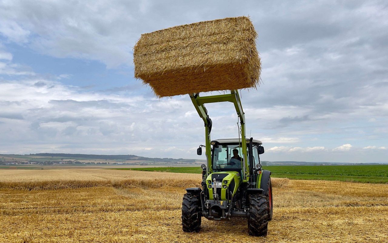 Claas Elios mit einem Strohballen am Frontlader.