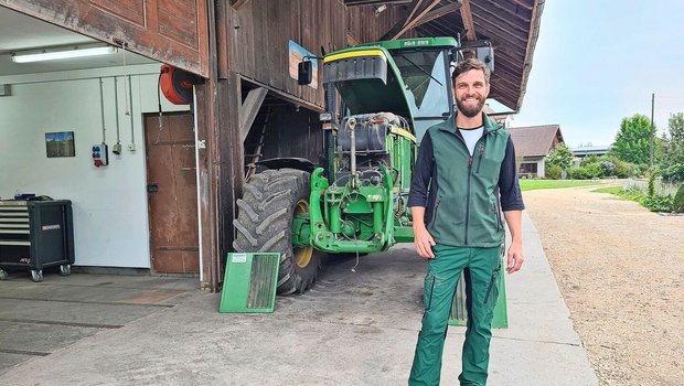 Lukas Streit steht auf dem Hofplatz, vor dem Traktor.