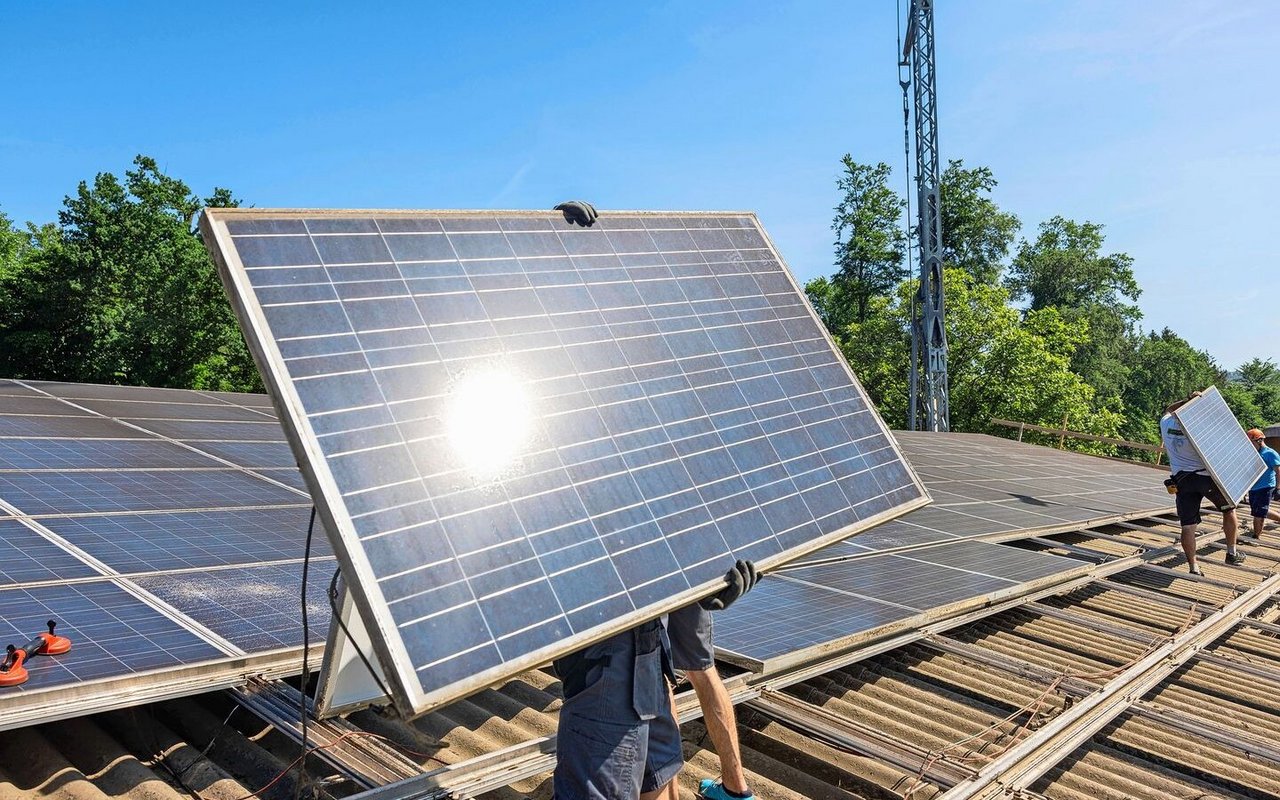 Ein Monteur trägt ein Solar-Panel, das er auf dem Dach montieren will.