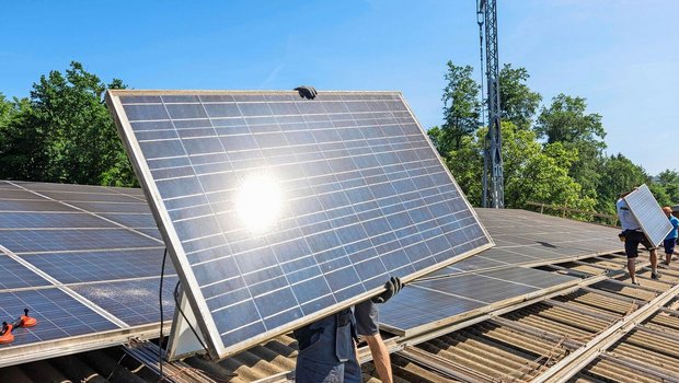 Ein Monteur trägt ein Solar-Panel, das er auf dem Dach montieren will.